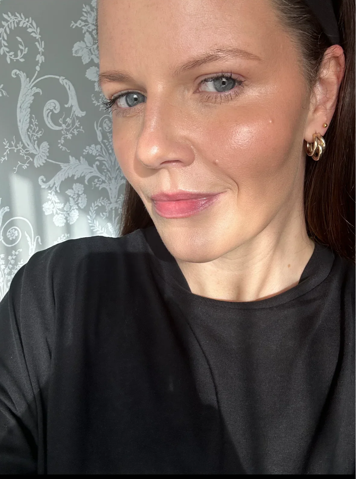 A woman with light skin and blue eyes smiles in natural light.