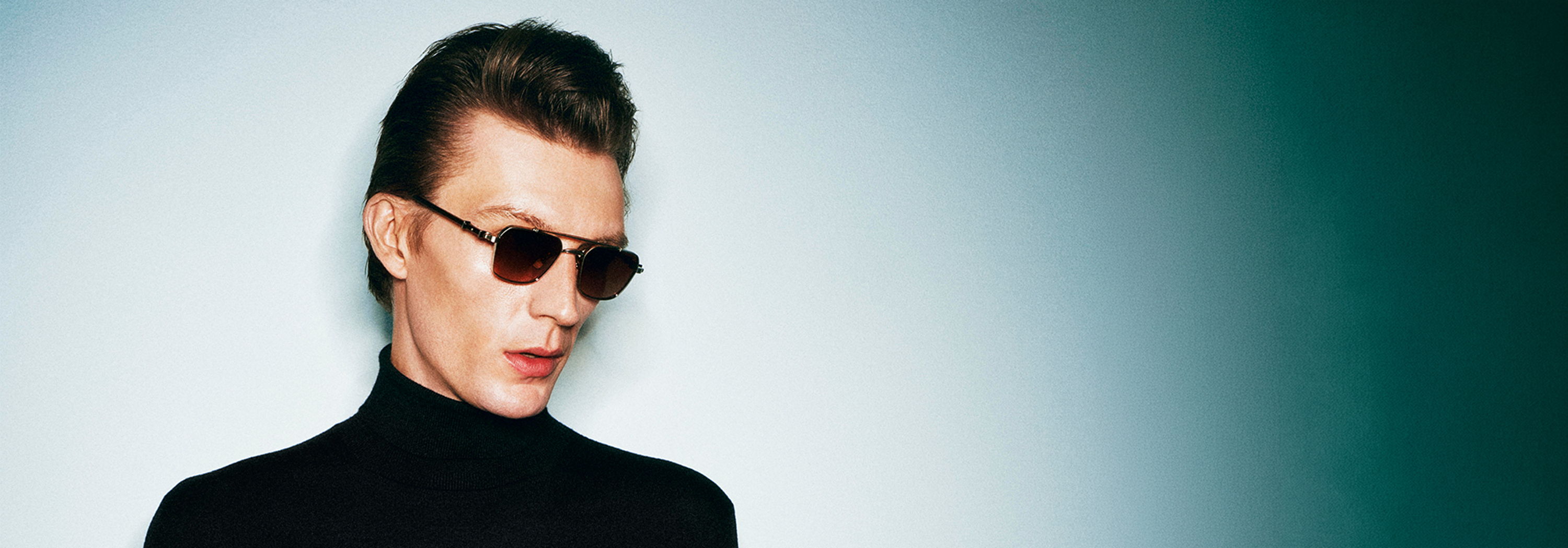 A person wearing Robert Marc sunglasses and a black turtleneck against a gradient background.
