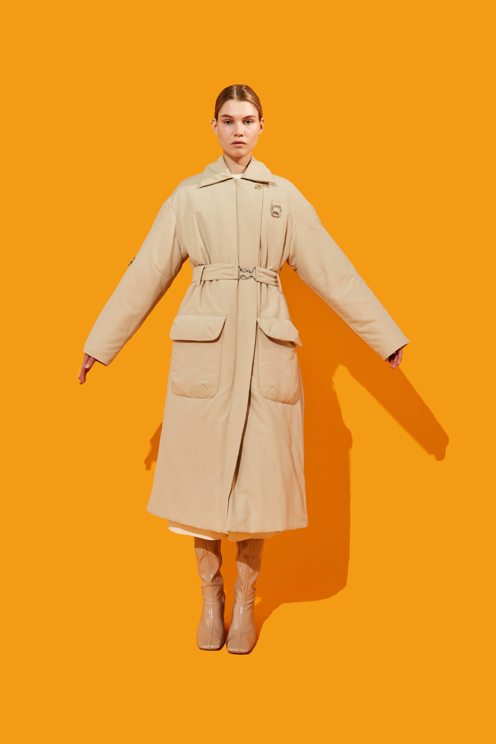 Model wearing a beige coat against an orange background.