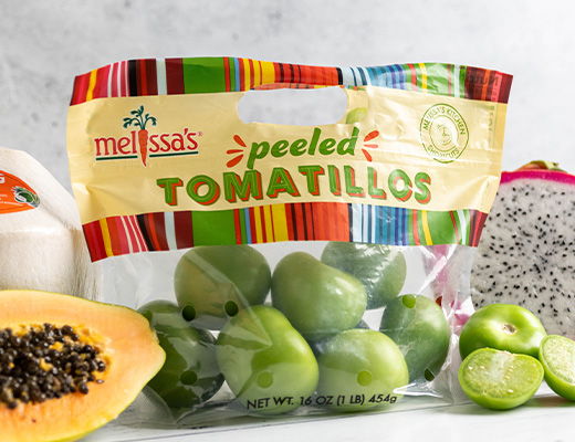 A package of peeled tomatillos with assorted fruits on a countertop.