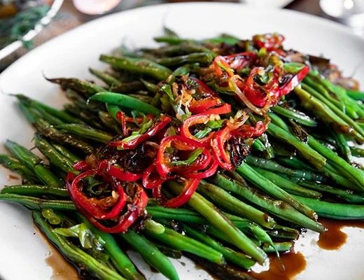 Plate of green beans topped with red peppers and sauce.