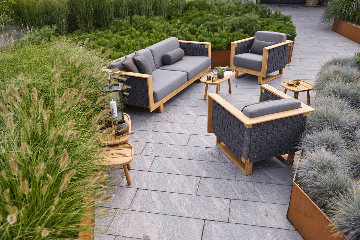 Teak framed outdoor lounge collection with plush cushions on a grass-lined patio.
