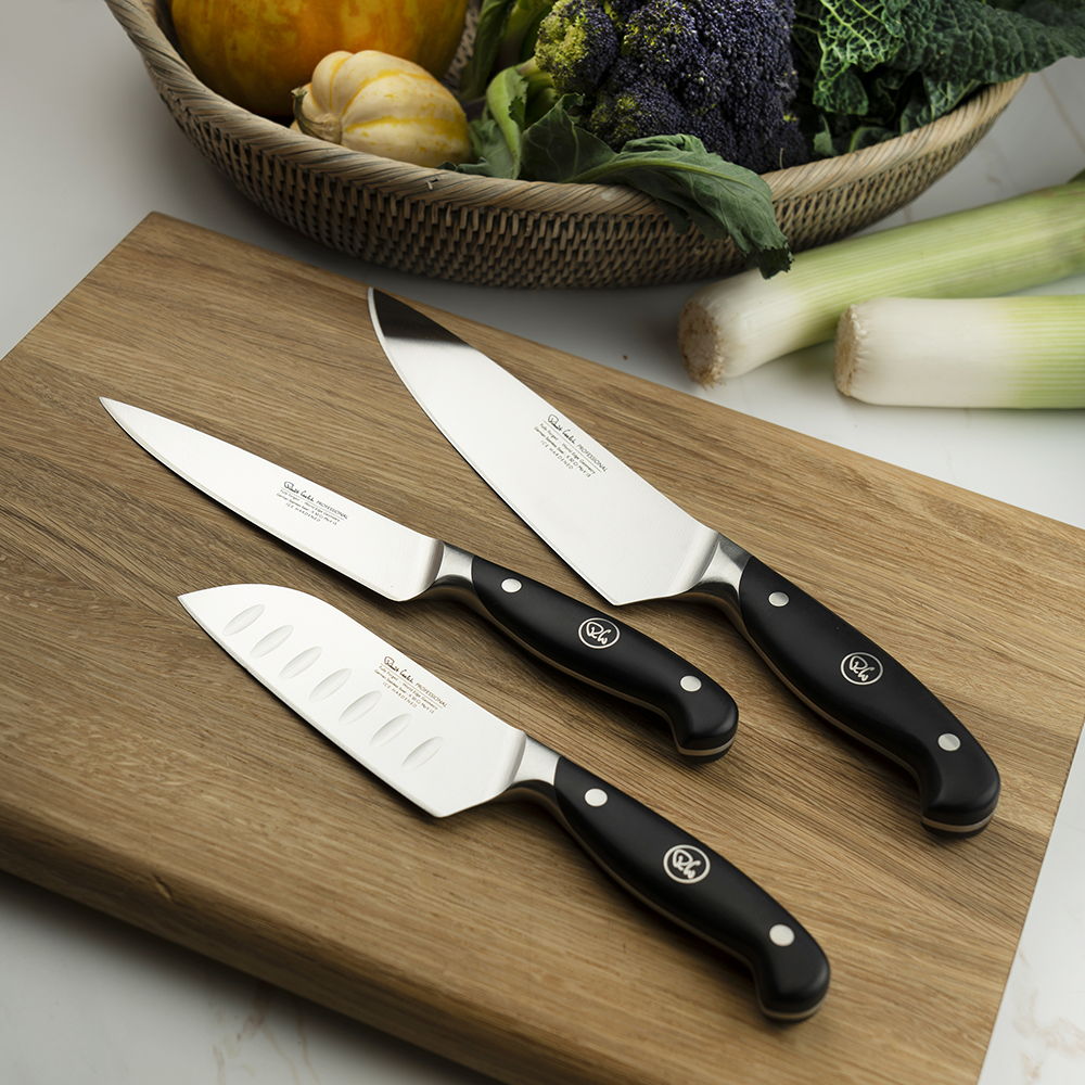 Professional Home Chefs Knife Set on a wooden cutting board with vegetables in the background.