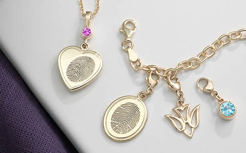 yellow gold heart shaped fingerprint necklace with a pink Swarovski birthstone bail and a yellow gold oval shaped fingerprint charm bracelet with a dove symbolic charm and blue Swarovski birthstone charm