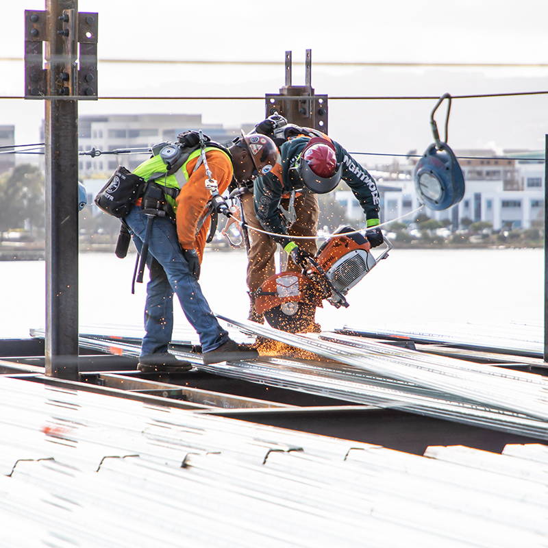 Two construction on metal decking sawing metal sheets wearing FallTech harnesses and self-retracting lifelines