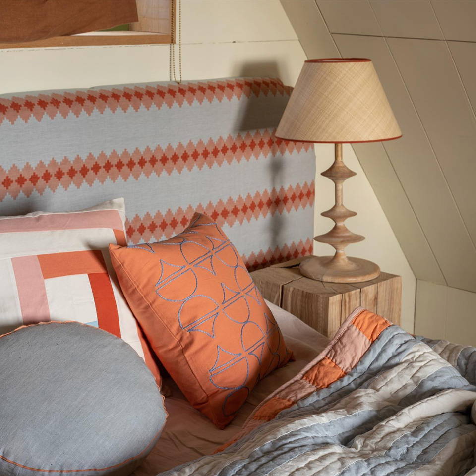 A close up of a bed in the treehouse covered with Campbell Collection cushions and quilt in blues and oranges.
