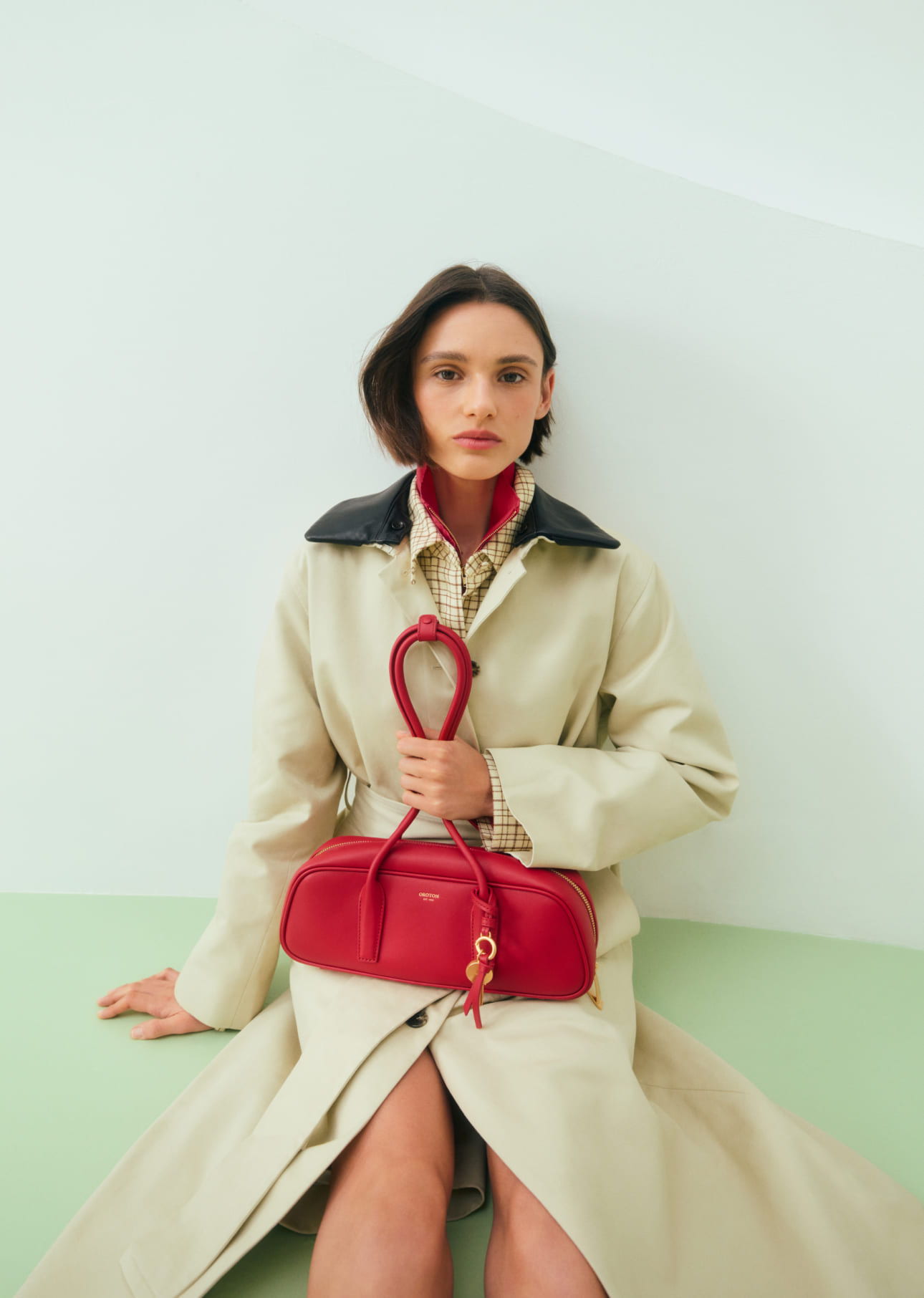 Woman in a beige coat holding a red handbag.