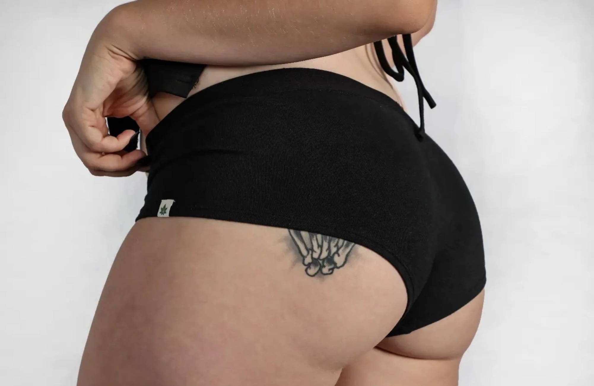 close-up of a woman’s tattooed butt wearing a black pair of undies