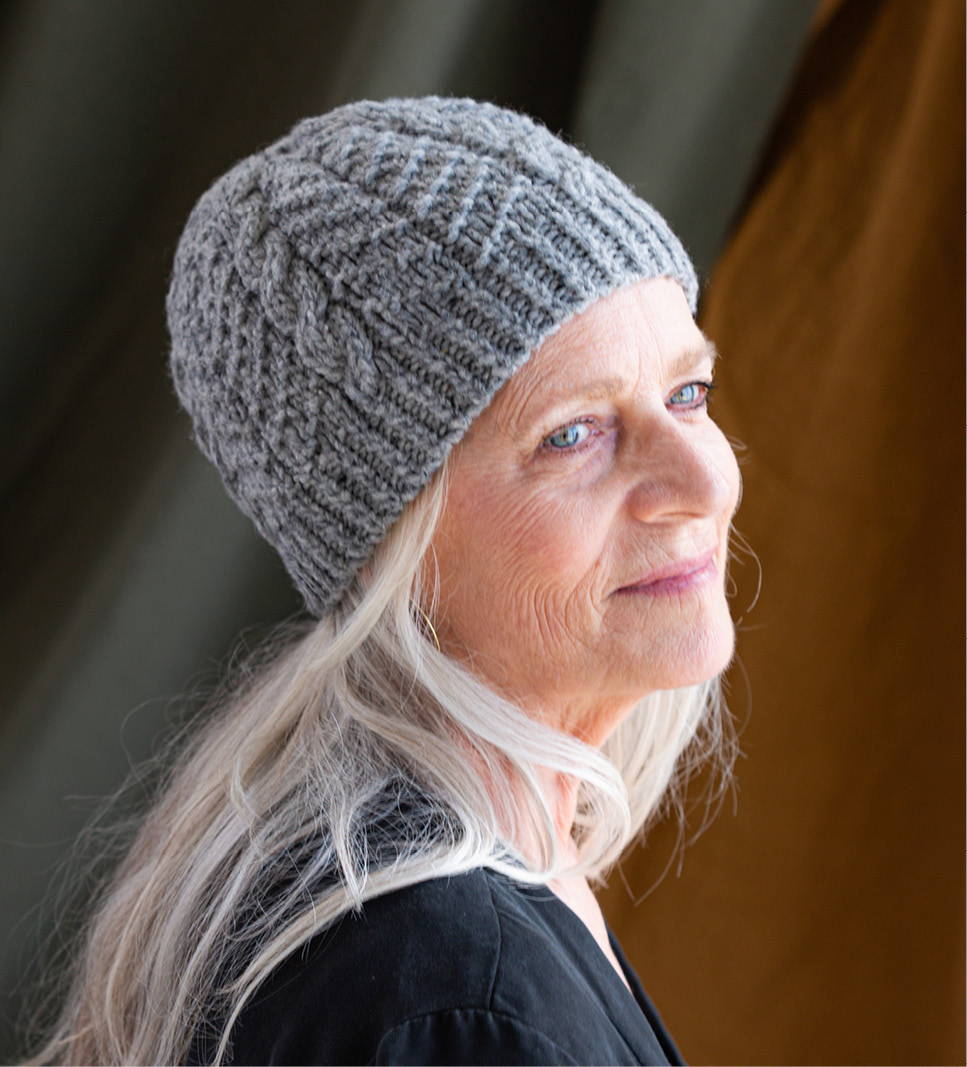 A gray-haired female model wears a hand knit chunky cabled beanie