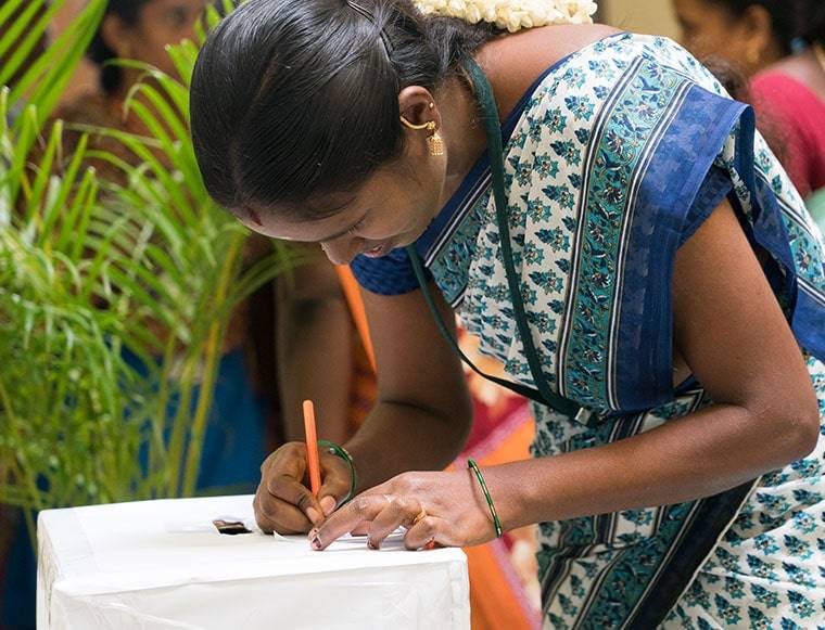 Woman writing down vote in ballot wearing colorful garments in a village in India.