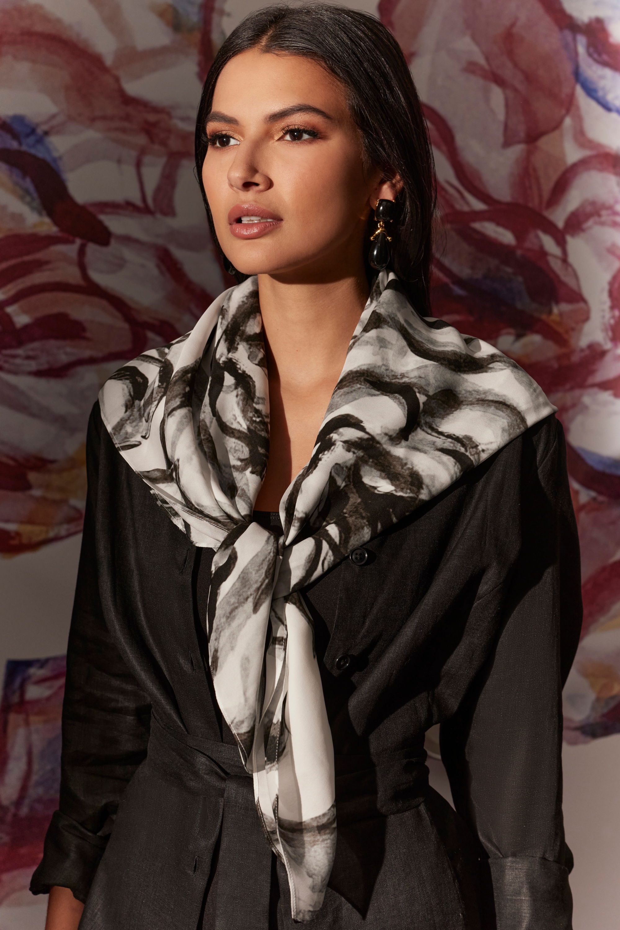 A woman wearing a black outfit and a patterned scarf, posing elegantly.