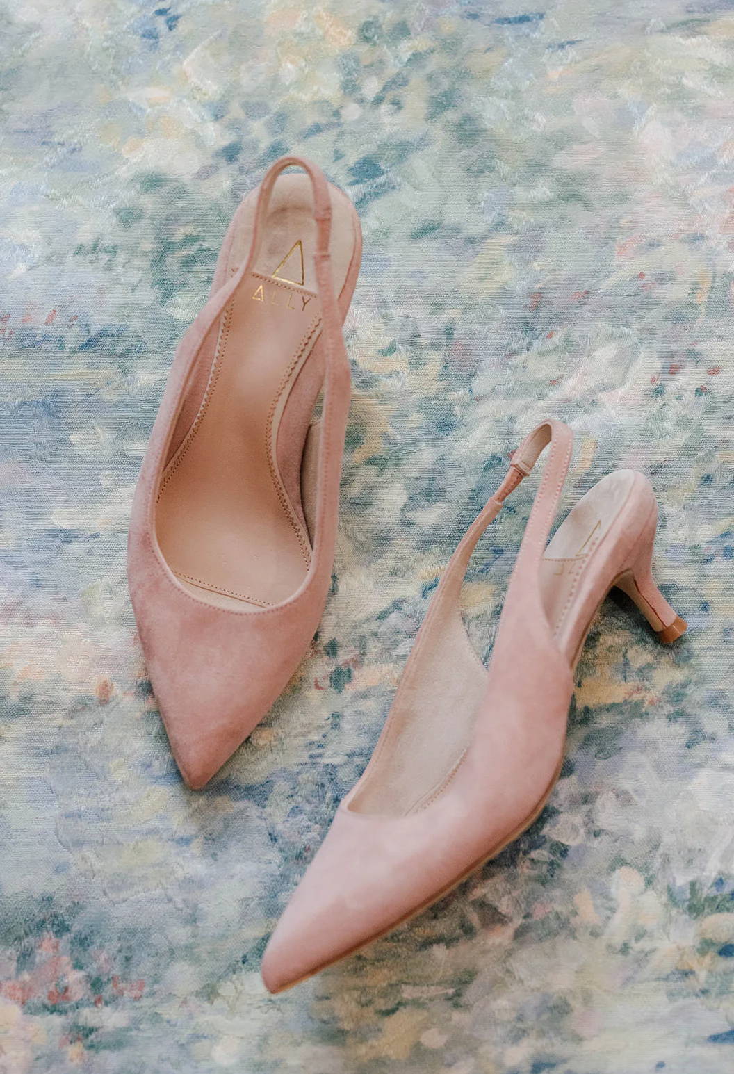 A pair of pink pointed-toe slingback heels on a textured surface.