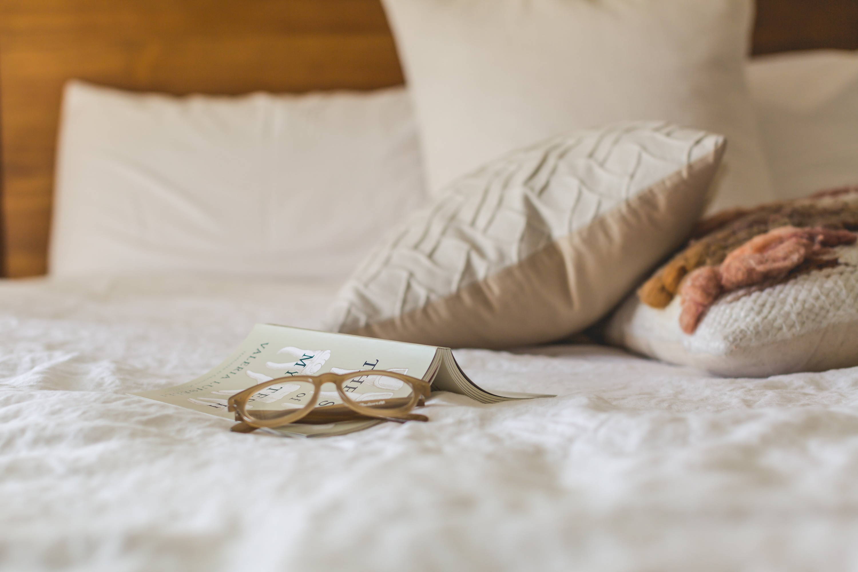 Bed with an open book and eyeglasses placed on the covers.