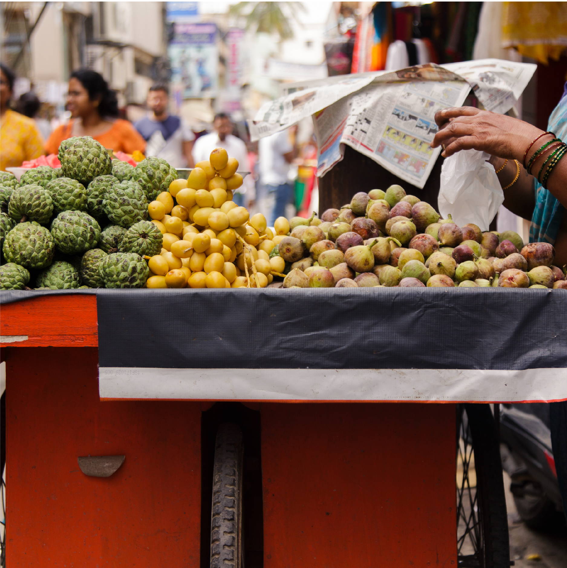 A street vendor on a crowded Bangalore India street, serves ripe figs, dates, and other fruits from her red bike-drawn cart