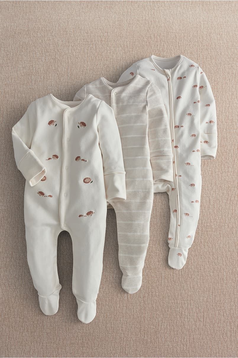 Three baby onesies laid out on a neutral background.