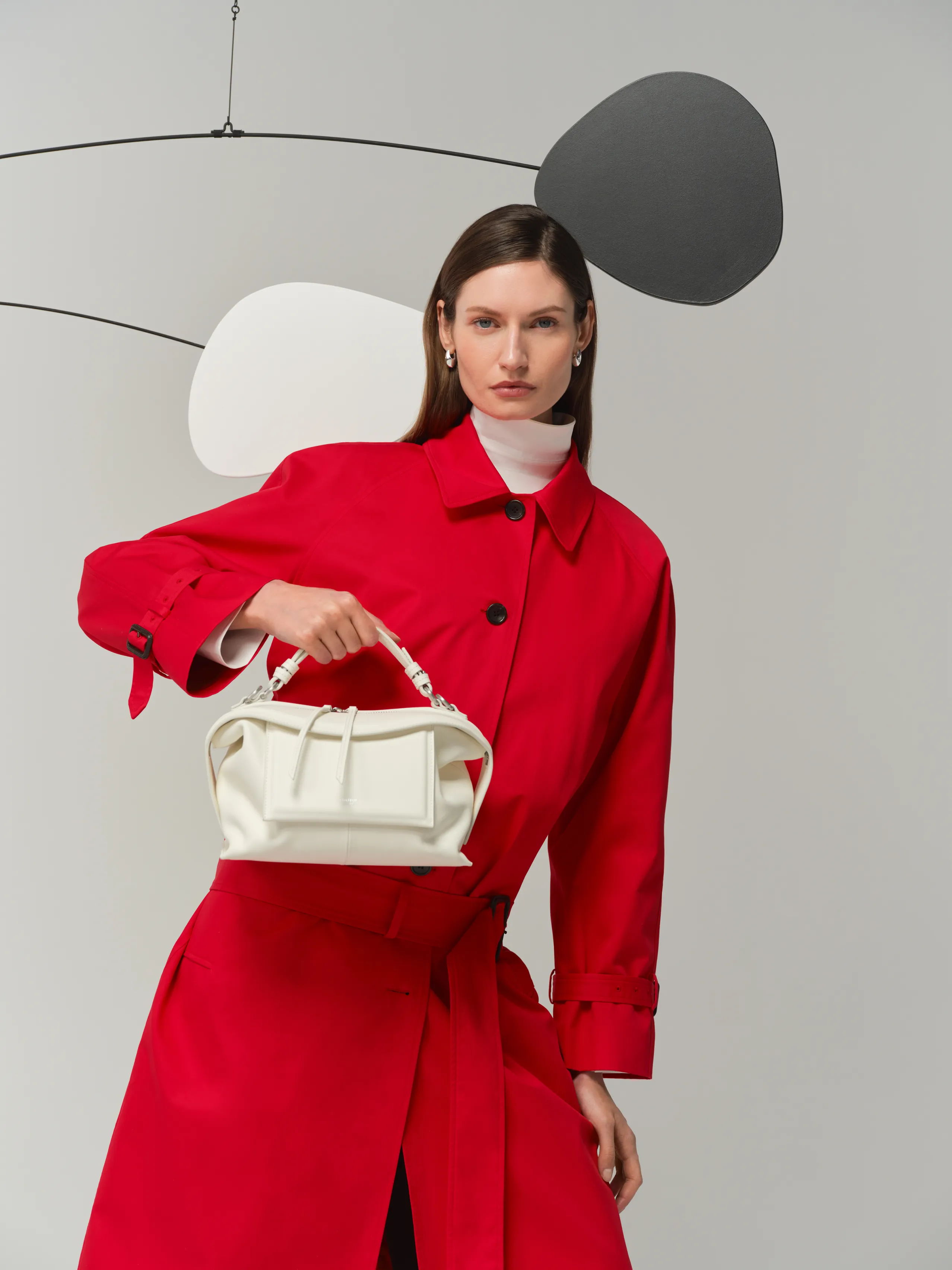 Model wearing a red coat holding a white handbag against a minimalist background.