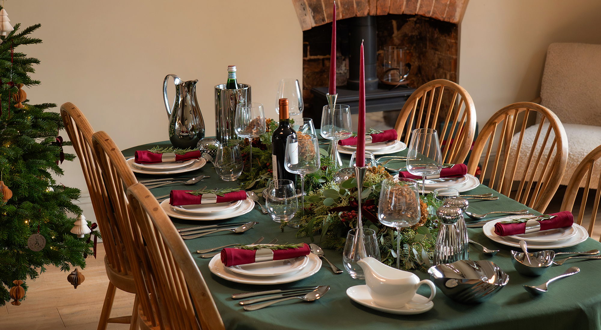 A festive dining table set for a holiday meal, decorated with greenery.