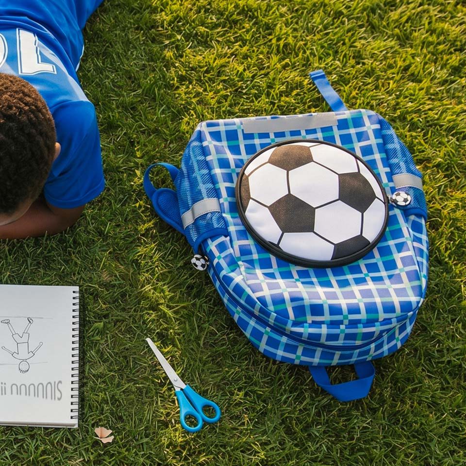 A child lying on grass with a blue backpack and drawing tools.
