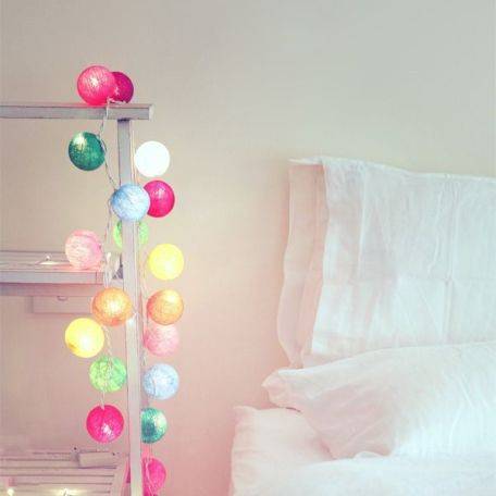 Multi coloured cotton ball fairy lights on a rack next to a bed.