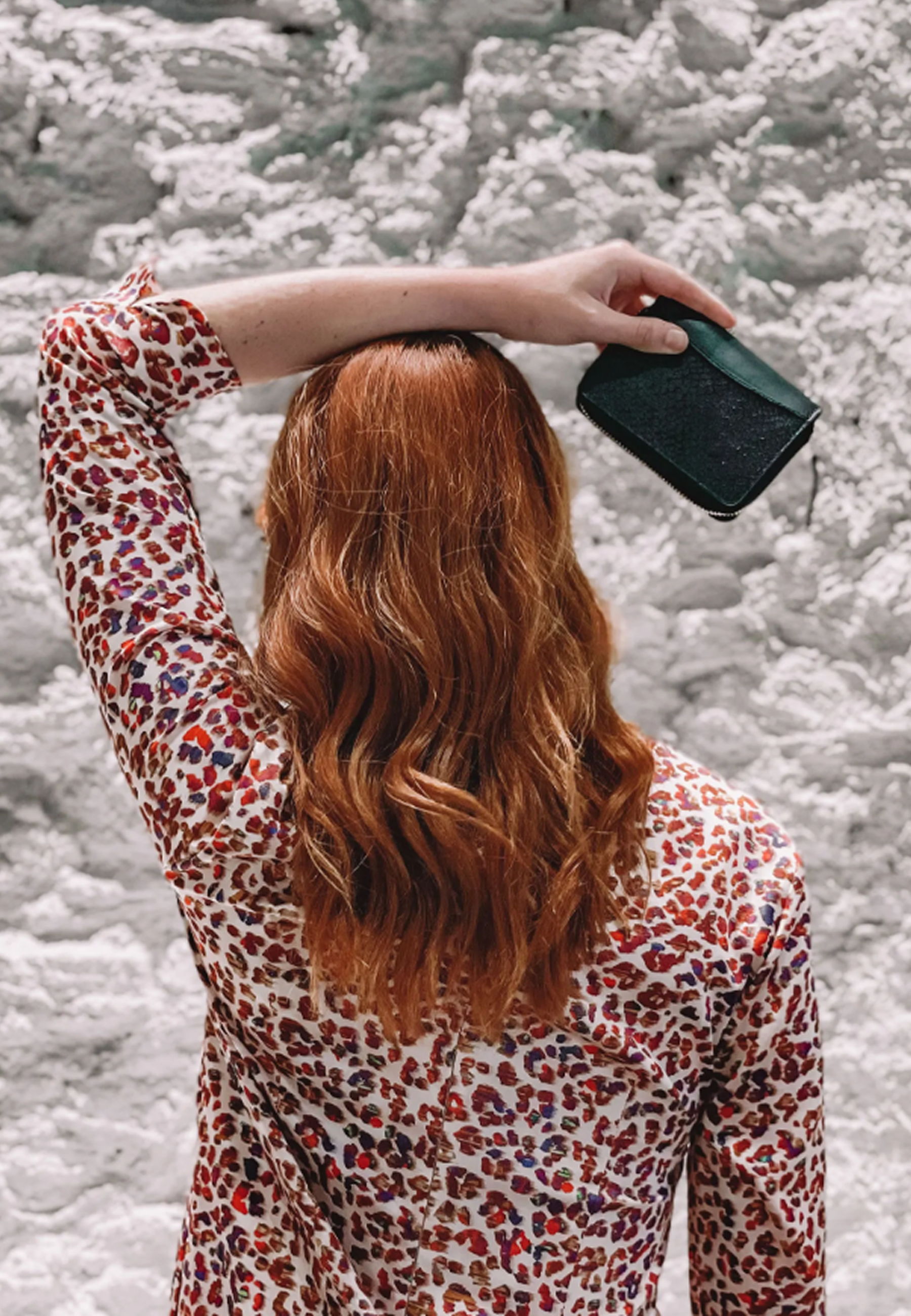Person with reddish hair holding a wallet against a textured wall.