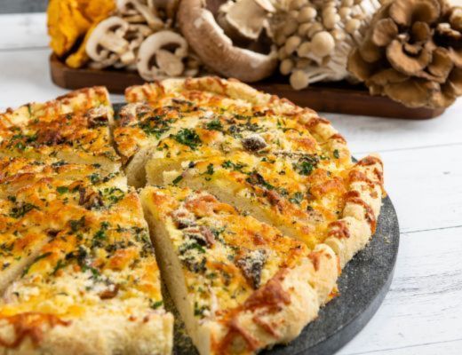 A sliced pizza with mushrooms and herbs on a wooden table.