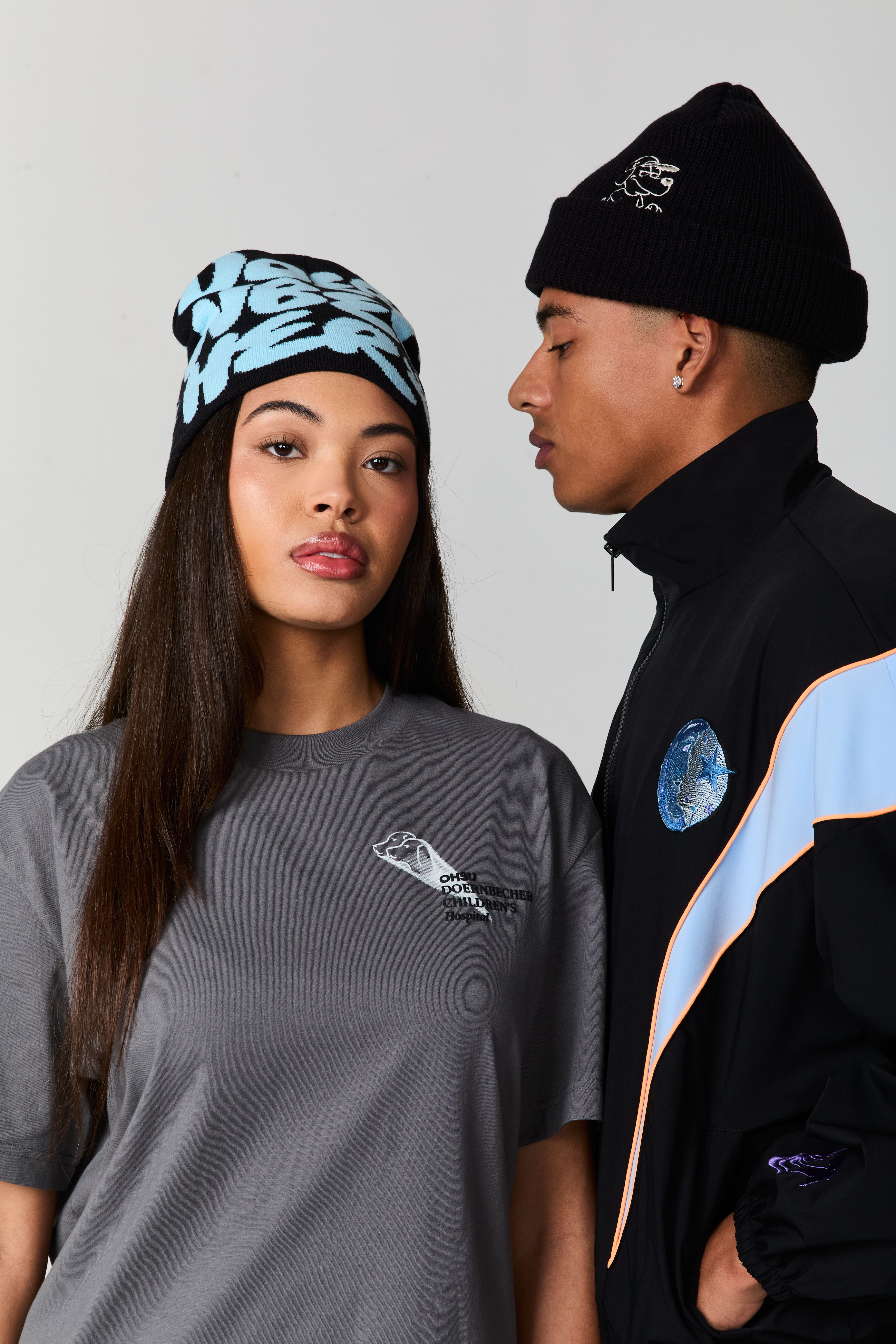 Two models wearing casual clothing and beanies, posing side by side.