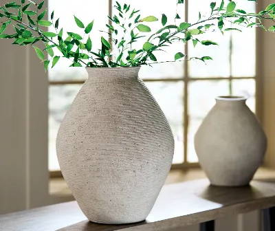 two cream vases are perched on a window with the sun bouncing off them. Greenery emerges from the vase in front.