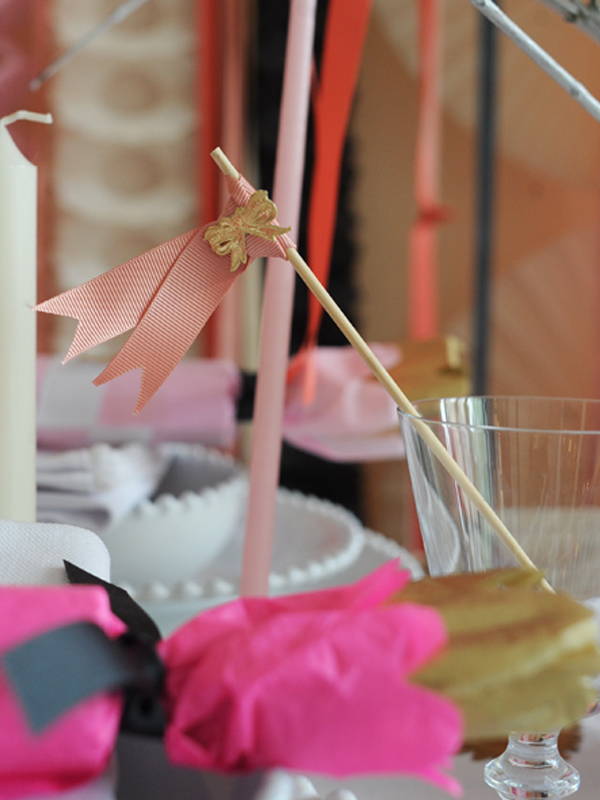 A close up of a wooden stick finished with a pink ribbon bow and a gold paper bow.