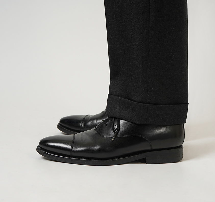 Black dress shoes with a tailored black suit pant leg.