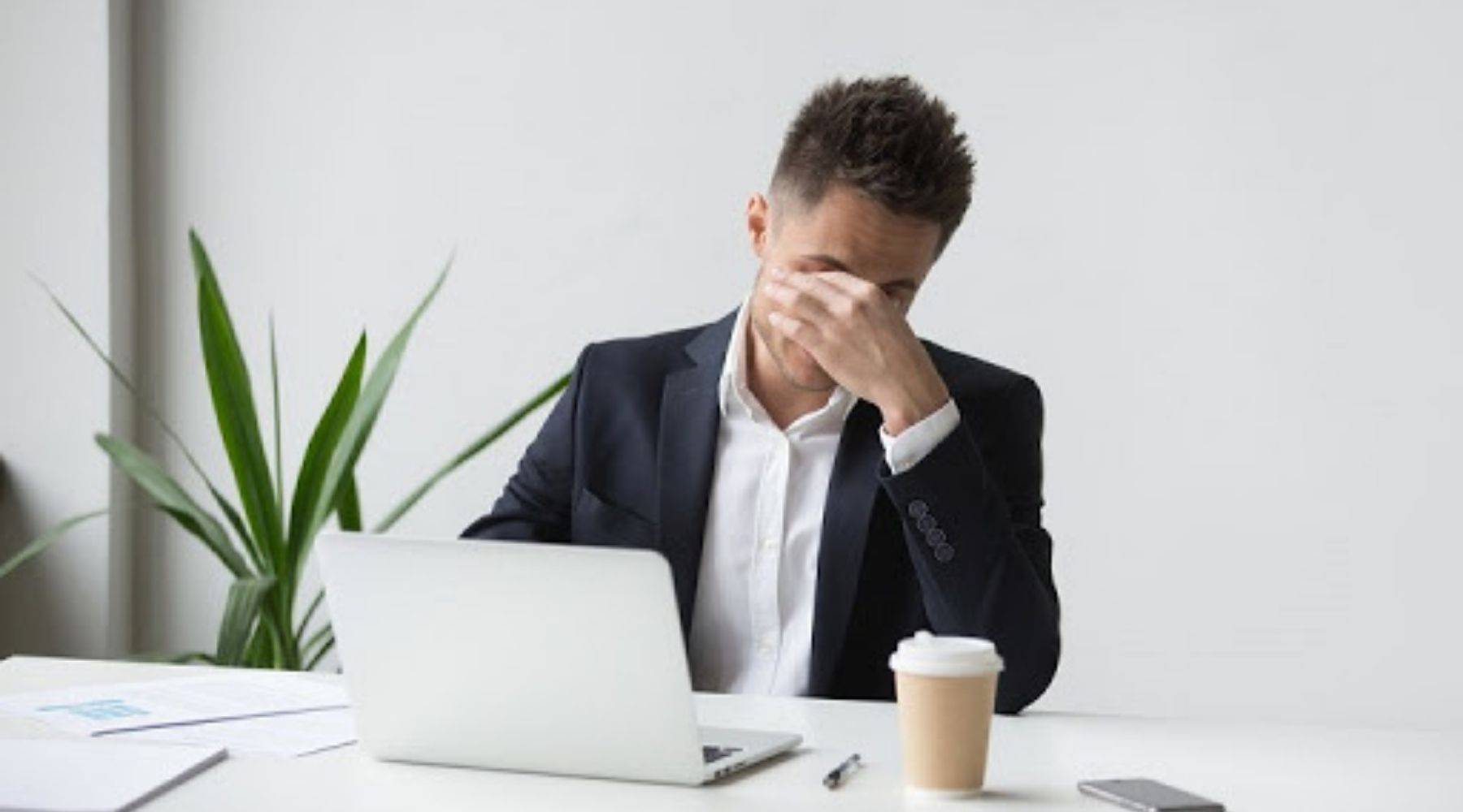 Homme assis devant un ordinateur montrant le syndrome de vision par ordinateur avec inconfort aux yeux et portant un costume buvant une tasse de café