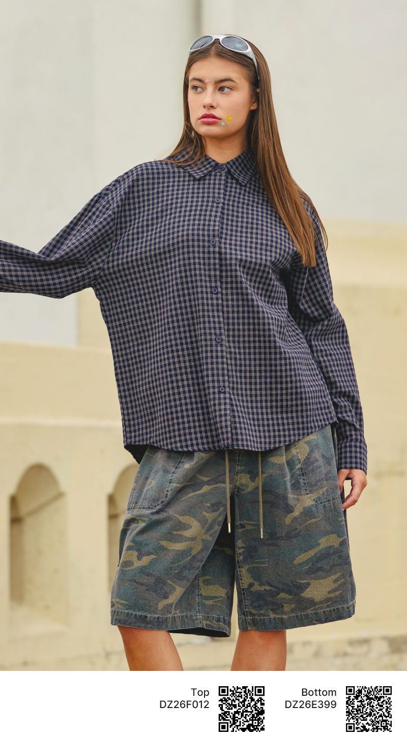 Woman wearing oversized checkered shirt and camo shorts, standing outdoors.