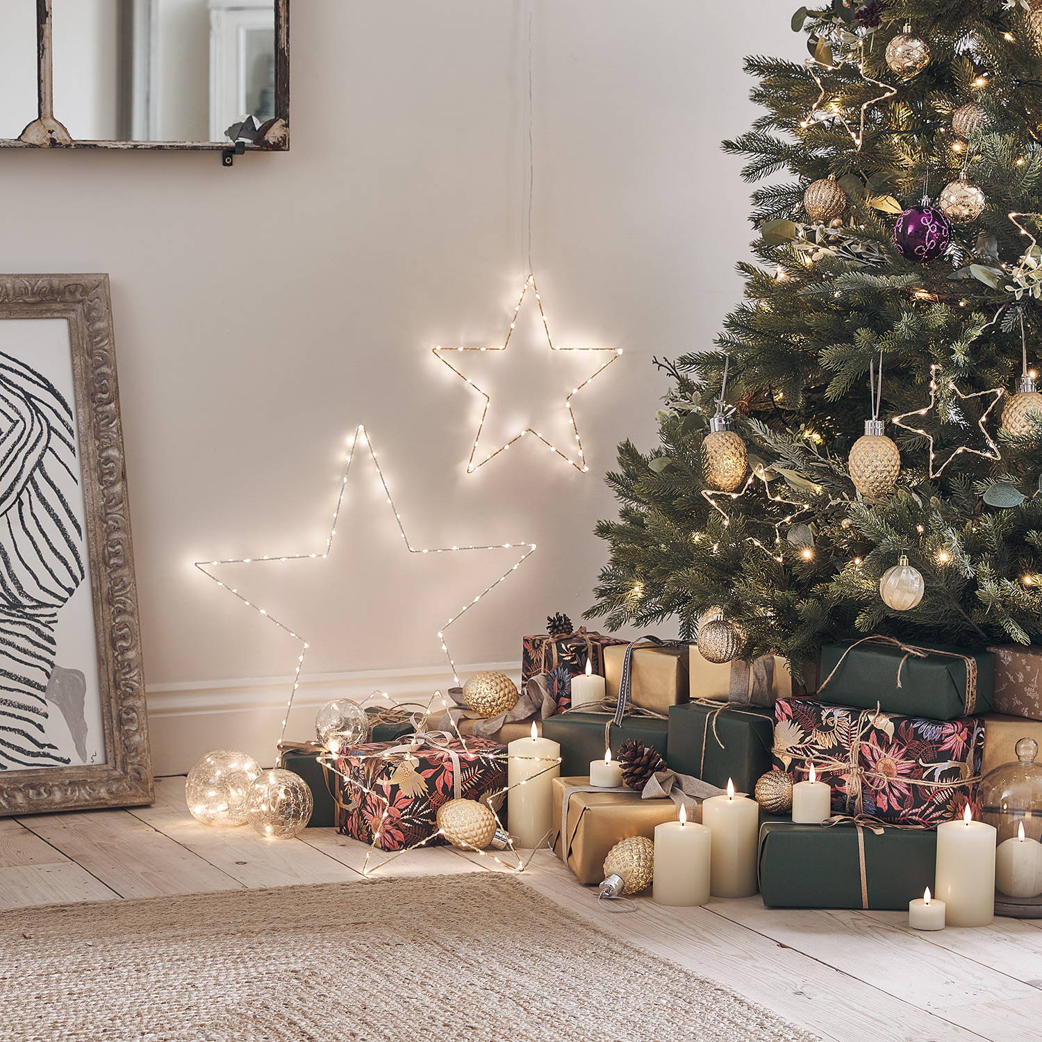 A close up of presents by a Christmas tree with LED candles nestled between them and Osby star lights on the wall.