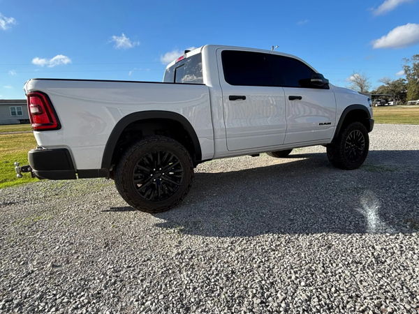 Rear three-quarter view of white RAM 1500 crew cab with black wheels on gravel lot