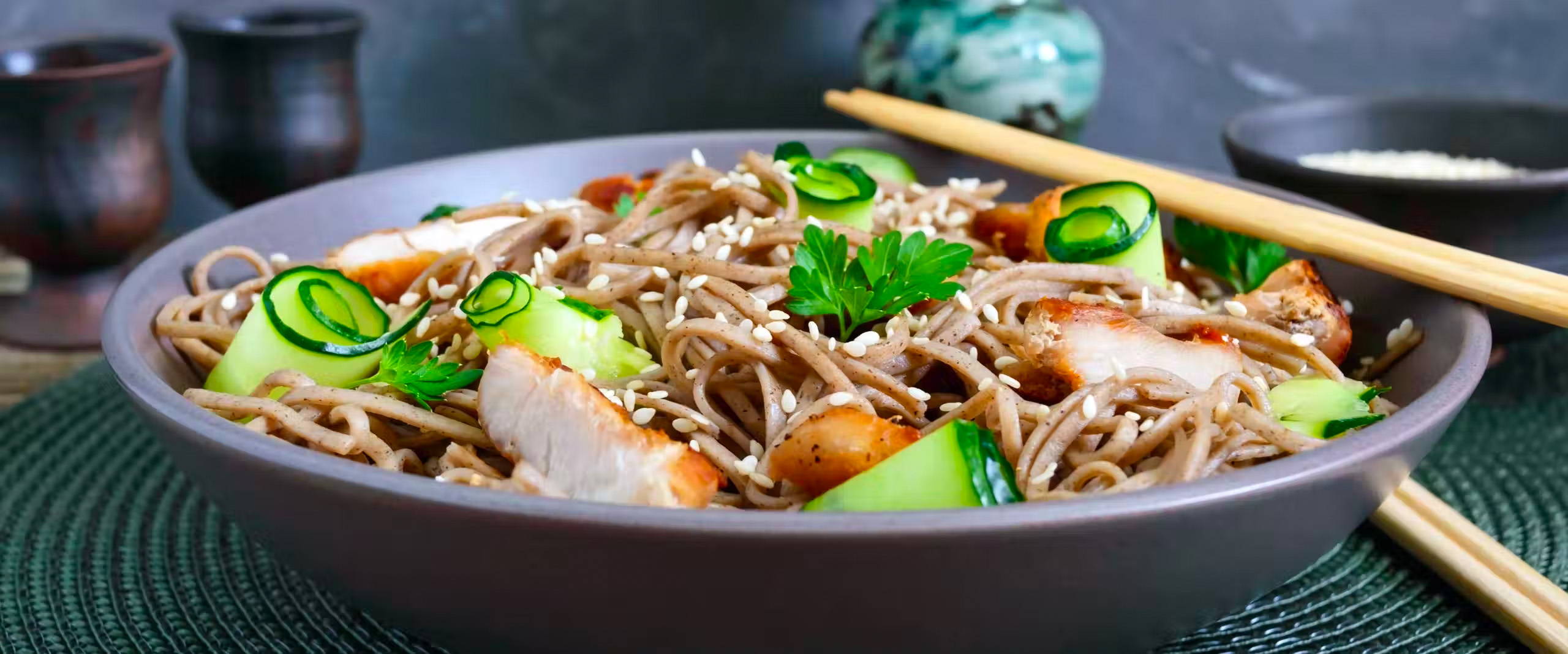 Bowl of sesame noodles with chicken, and chop sticks on the side.