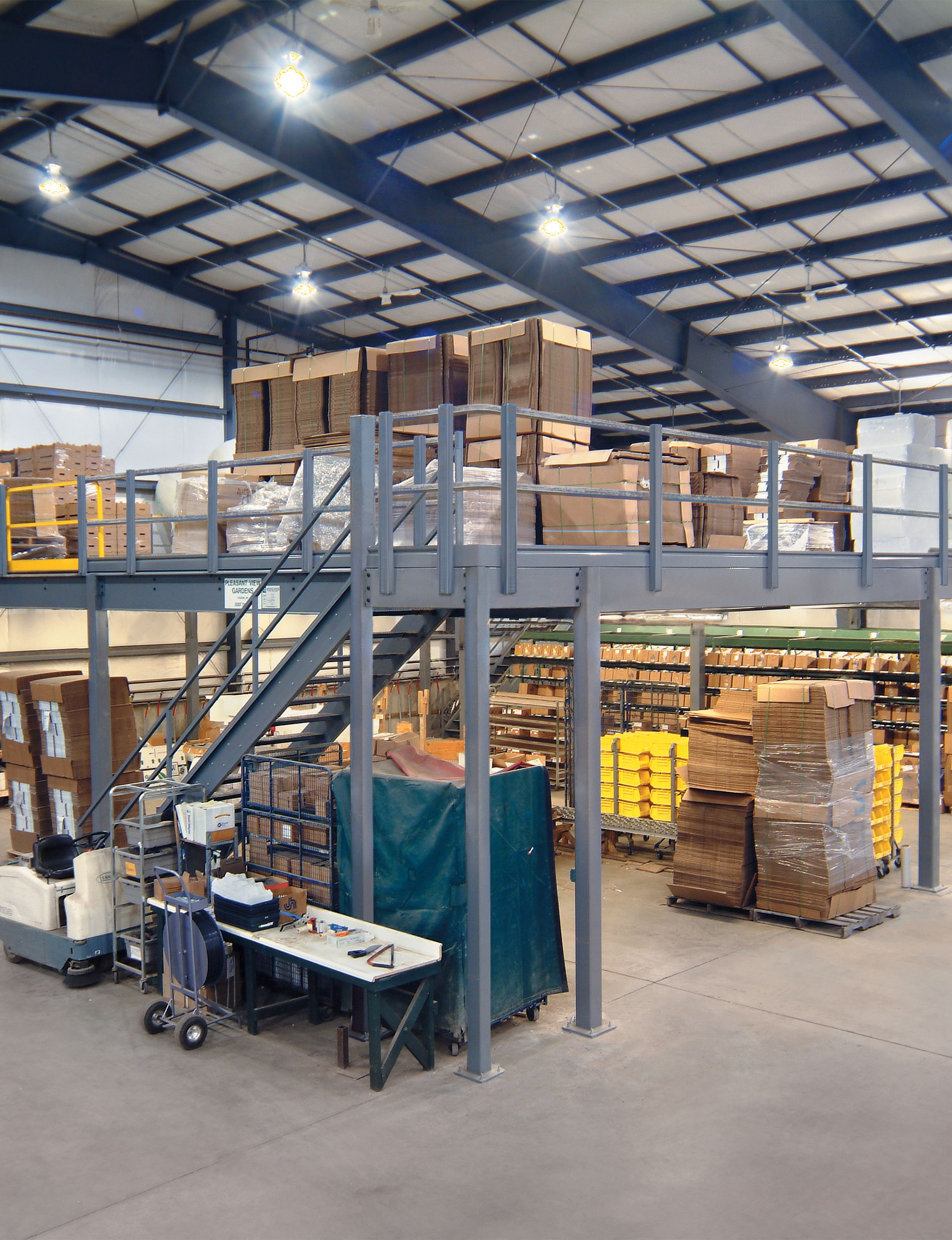 Warehouse interior with stacked boxes, stairs, and worktables.