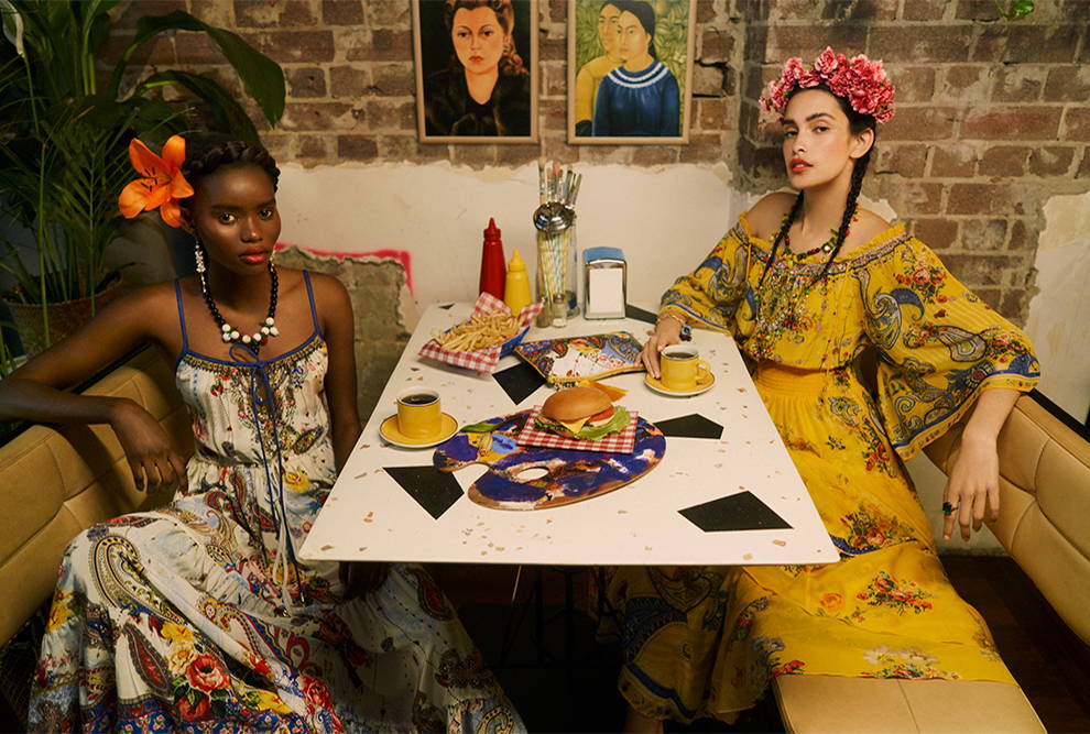 Two models sitting at a table in bright dresses