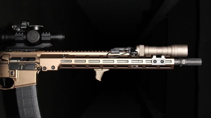 A close-up of a tactical firearm with a scope and suppressor.
