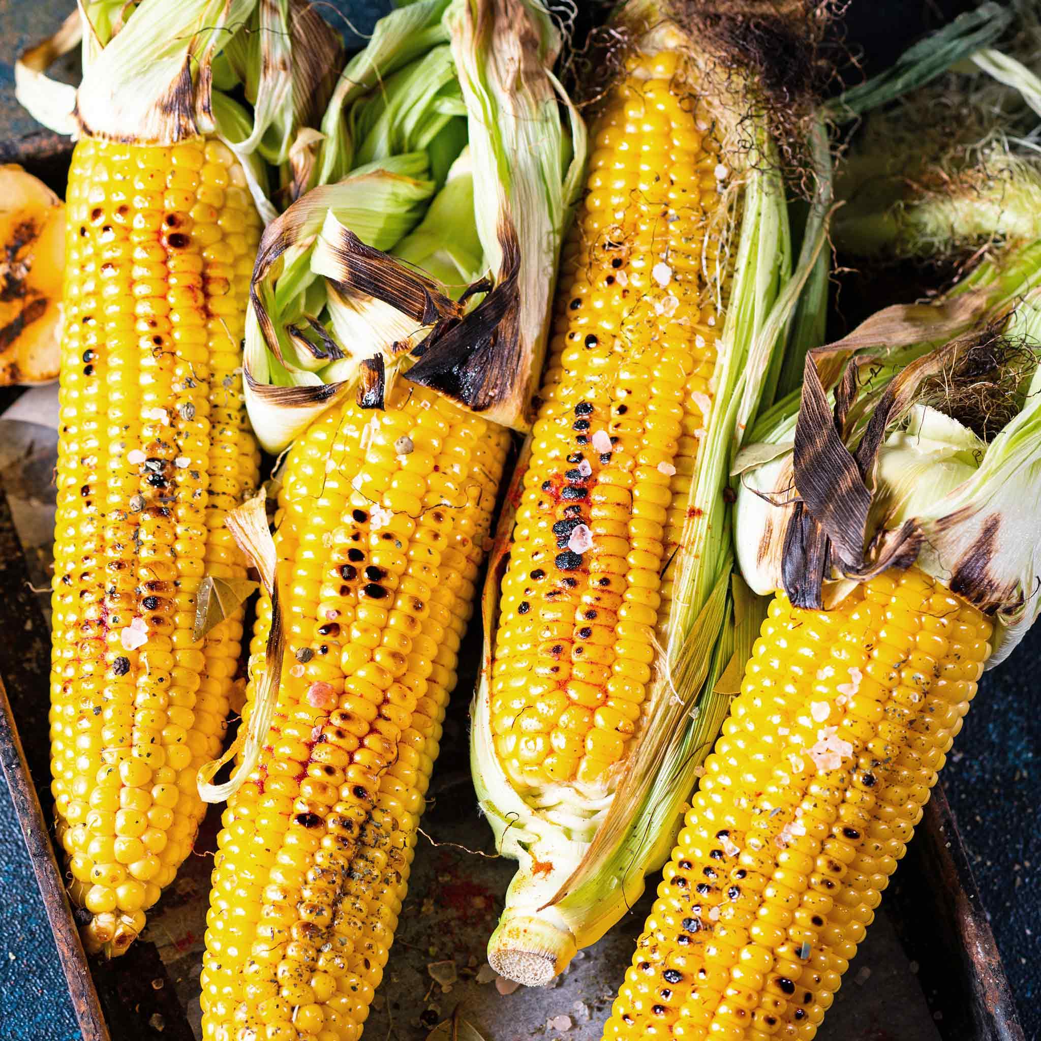 Roasted sweetcorn cobs on a tray, with char marks and seasonings visible.