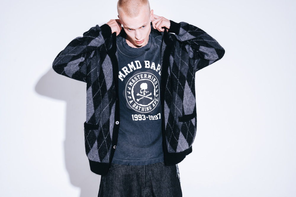 Young man in a patterned hoodie and graphic t-shirt against a plain background.