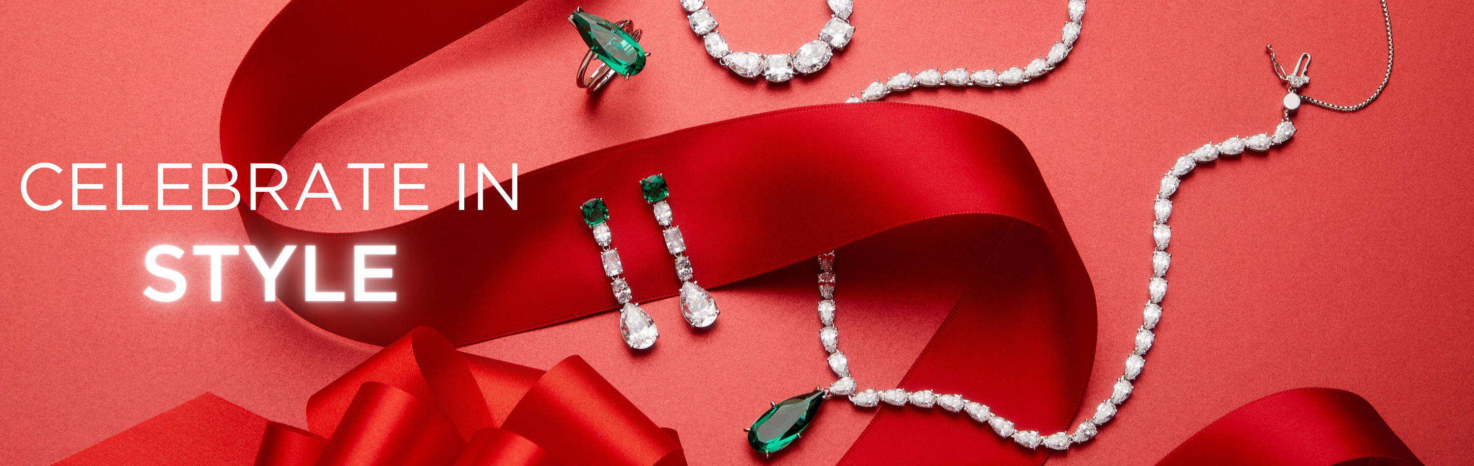 Celebrate in style. Image of cubic zirconia and emerald green colored necklace, earrings, and ring on red wrapping paper and red bow. 