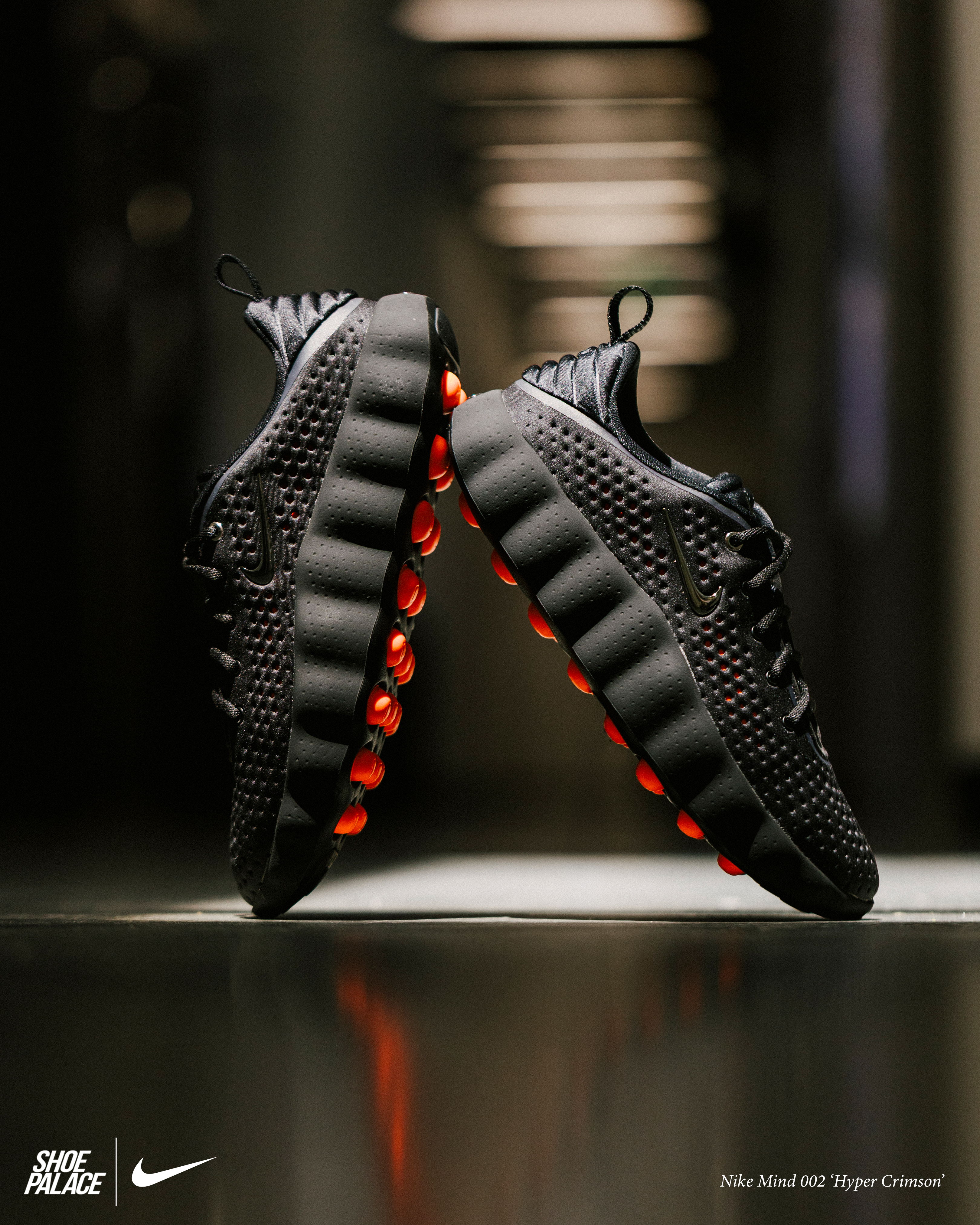 Black Nike sneakers with red accents on a reflective surface.