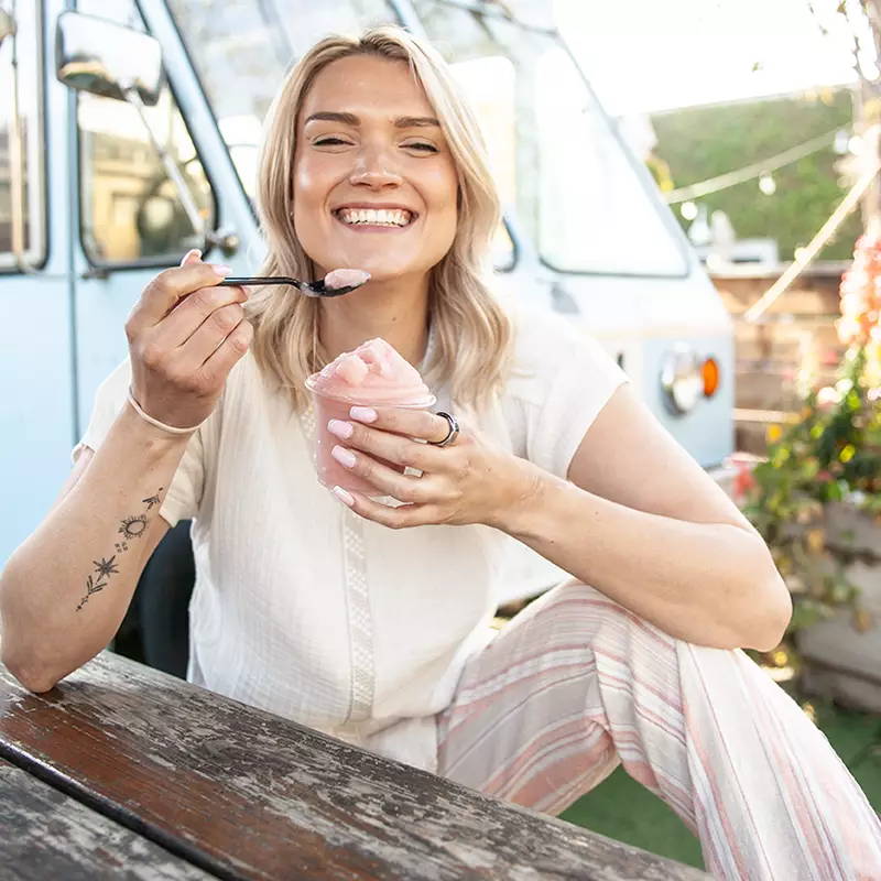 Woman sitting on wooden table eating ice cream.