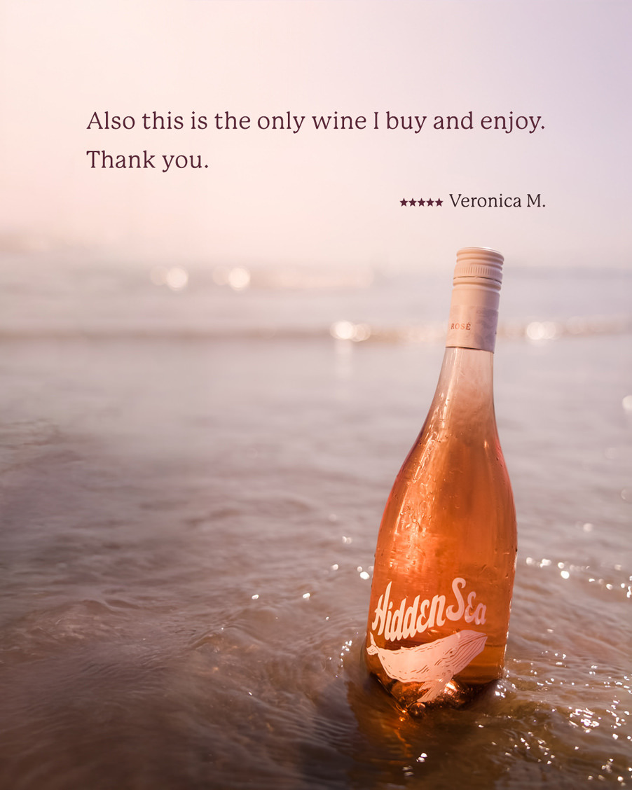 A The Hidden Sea rosé bottle standing in shallow water with a 5-star review quote: “Also this is the only wine I buy and enjoy. Thank you.” — Veronica M.