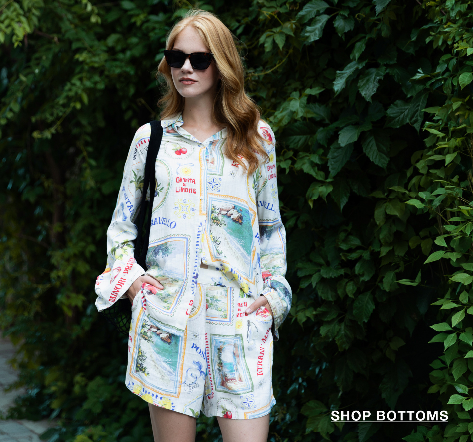 Woman in patterned outfit standing against greenery, wearing sunglasses.