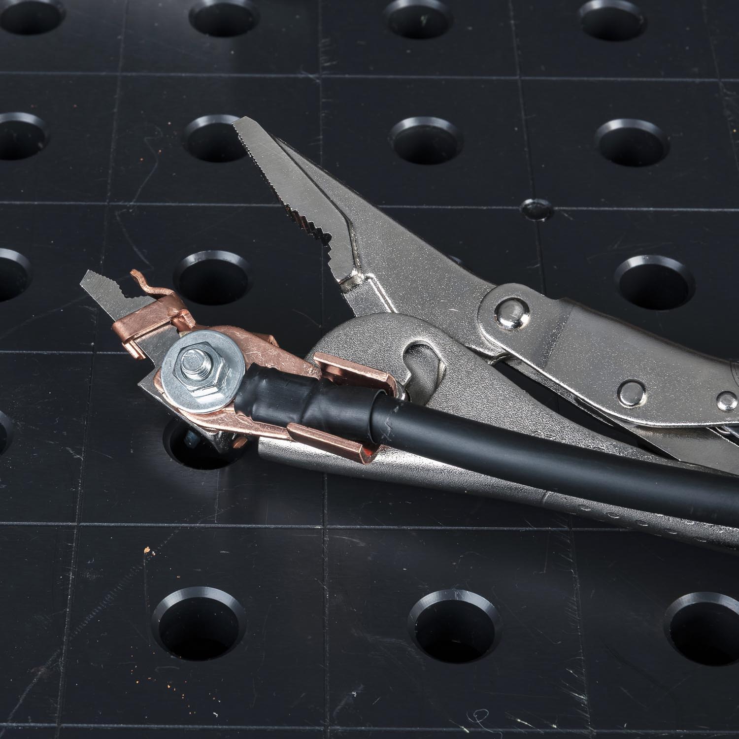 Pliers holding a wire connection on a black perforated surface.