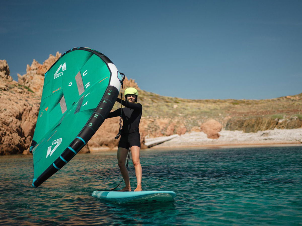 Person on a surfboard holding a green kite in clear water.
