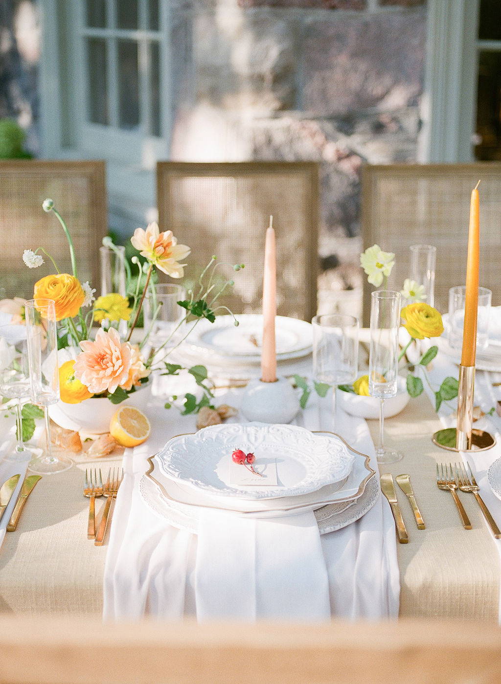 wedding table scape with white plate with two cherries, small orange and peach floral arrangement,  glassware, and orange and peach candles
