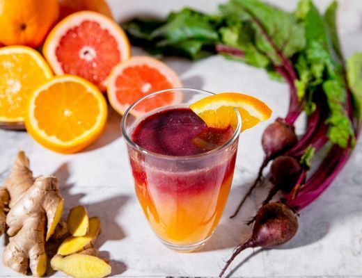 A colorful drink surrounded by oranges, beets, and ginger on a table.