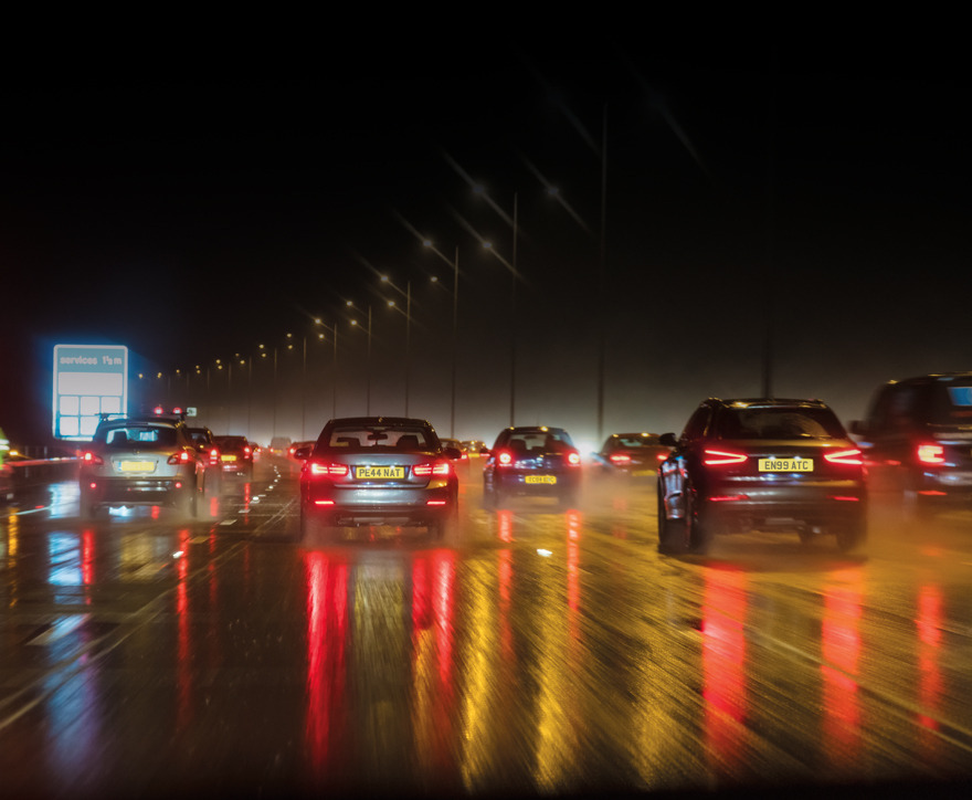 Cars driving on a wet road at night, reflecting lights.