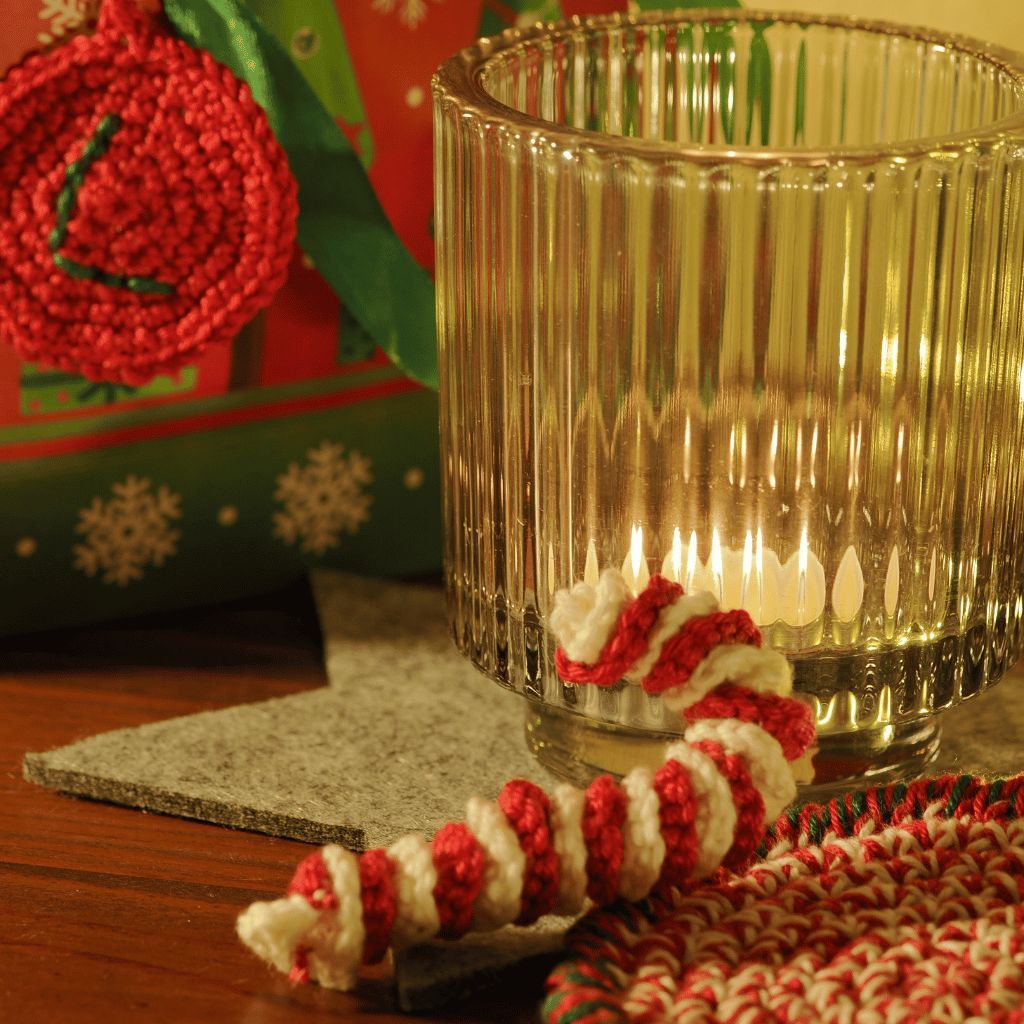 Gehäkelte Weihnachtsdekoration und eine brennende Kerze auf einem Holztisch.
